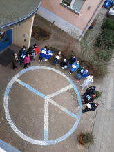 Peace-Zeichen aus Kreide, Menschen stehen in Halbkreis drumherum