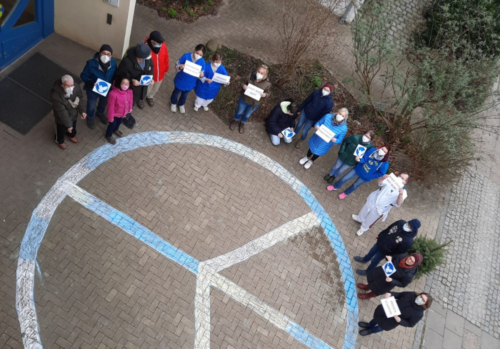 Peace-Zeichen aus Kreide, Menschen stehen in Halbkreis drumherum